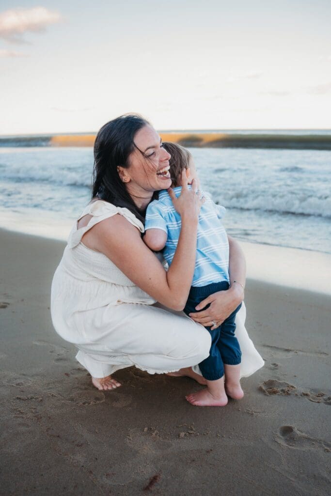 Parents holding toddler while expecting their next child, photographed at Salisbury Beach in Massachusetts
